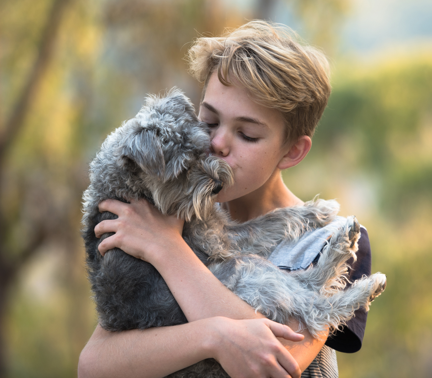 A young boy holding is dog in his arms kissing it